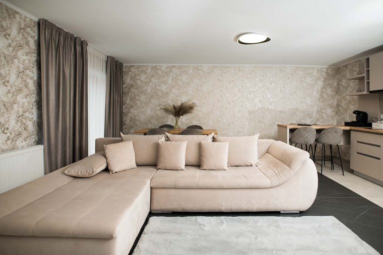 A living room with a beige couch and a kitchen available for rezervare in Cisnadie, offering cazare.