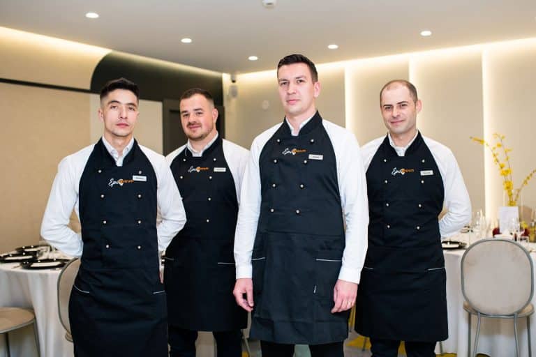 Four men in black aprons standing next to each other at a hotel.