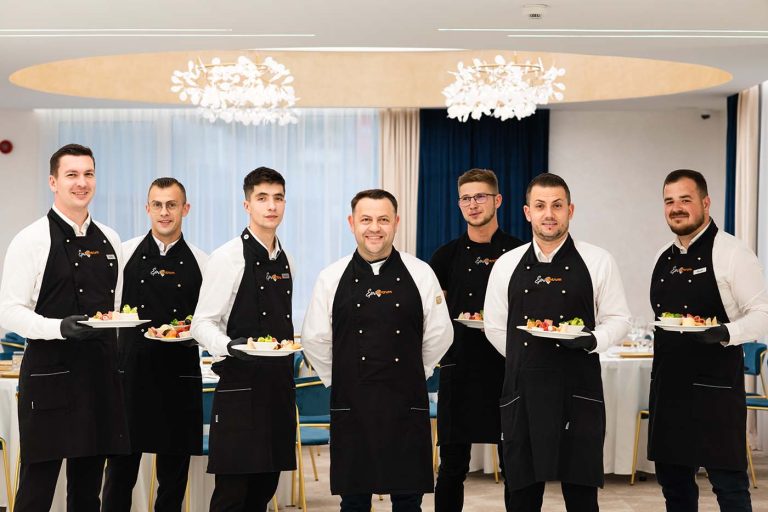 A group of men in black aprons serving food at a hotel.