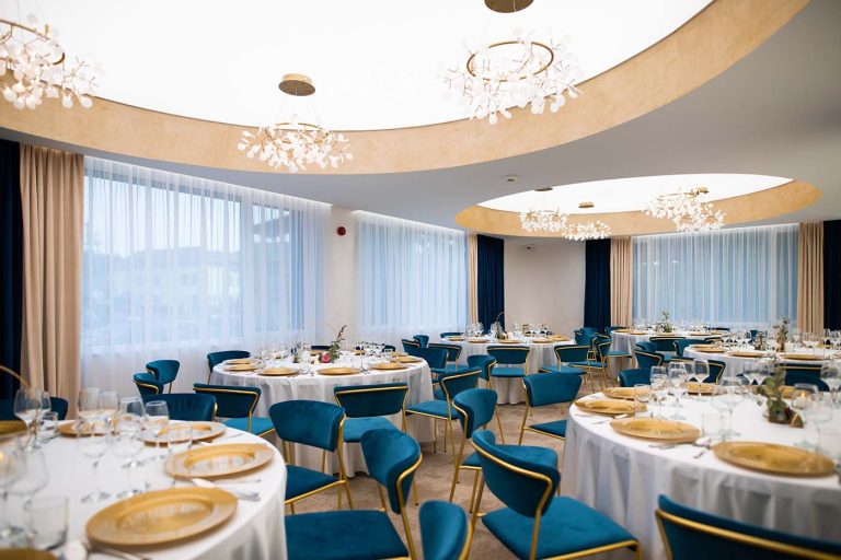A hotel banquet room with blue chairs and chandeliers available for reservation in Cisnadie.