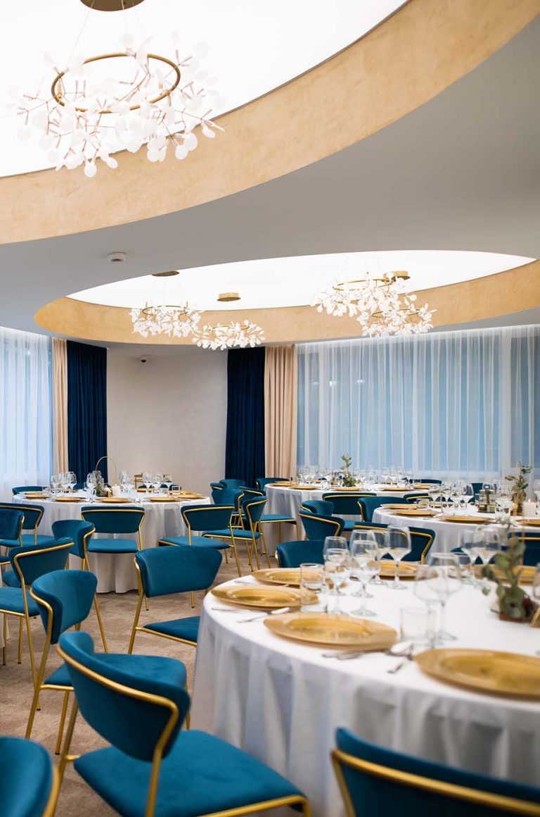 A banquet room with blue chairs and a chandelier available for booking at a hotel in Cisnadie.