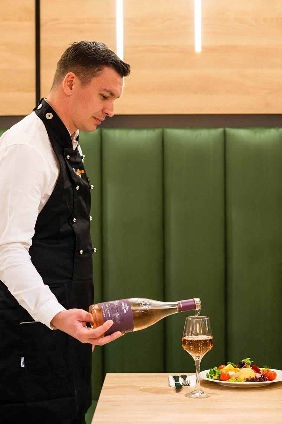A chef pouring a bottle of wine on a hotel table.