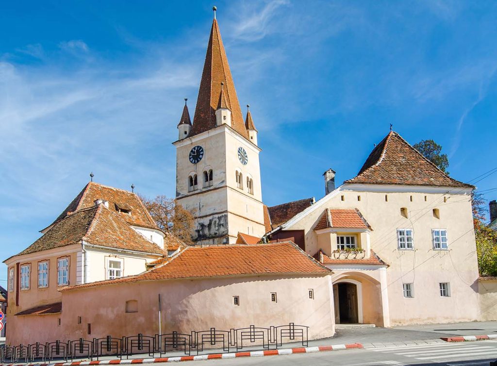 A church with a clock tower in the middle of a street, captured through a camera lens.